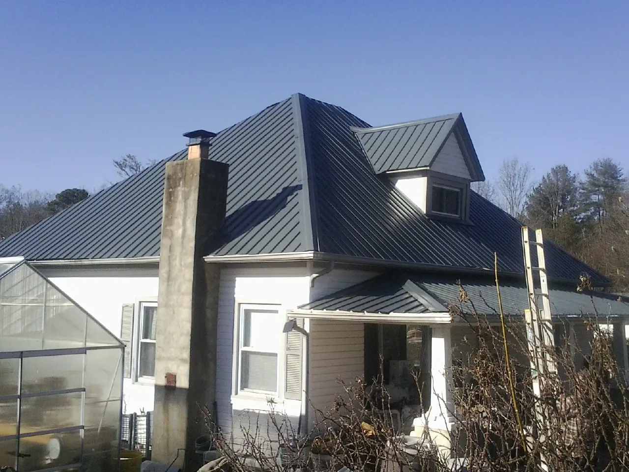 Dark blue standing seam metal roof on a white farmhouse with dormer — Slate & Tile Roof Repair by Roofing Brothers in Sun Valley