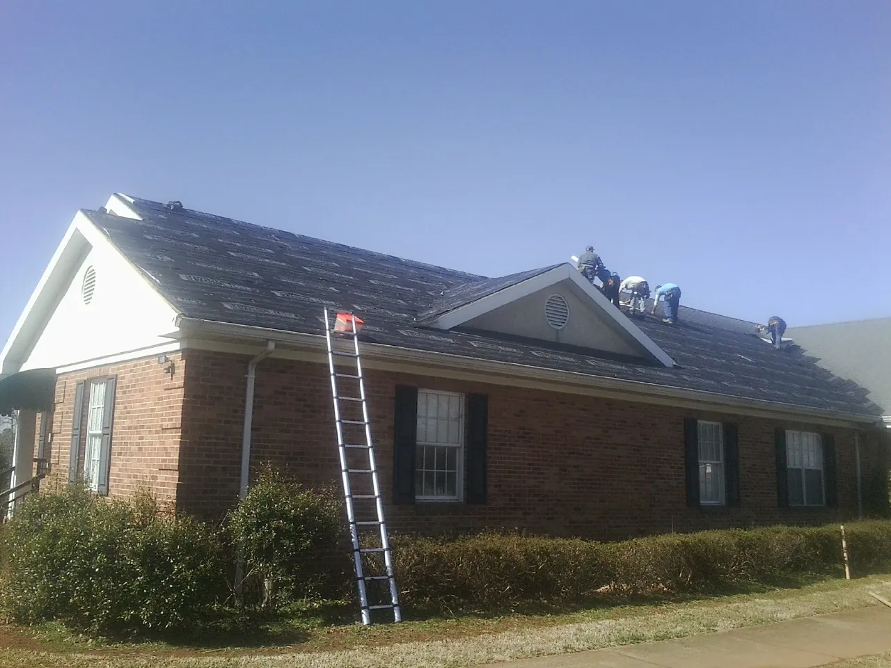 Crew tearing shingles off a brick ranch roof with a ladder set — Emergency Roof Repair work by our crew in Sun Valley