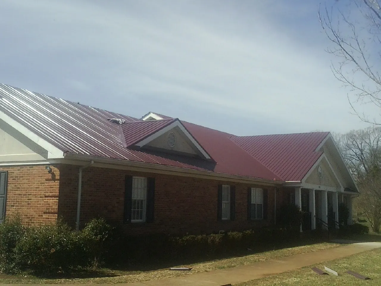 Red metal roof with gabled entries on a long brick building, from a Hail Damage Roof Repair job in Sun Valley