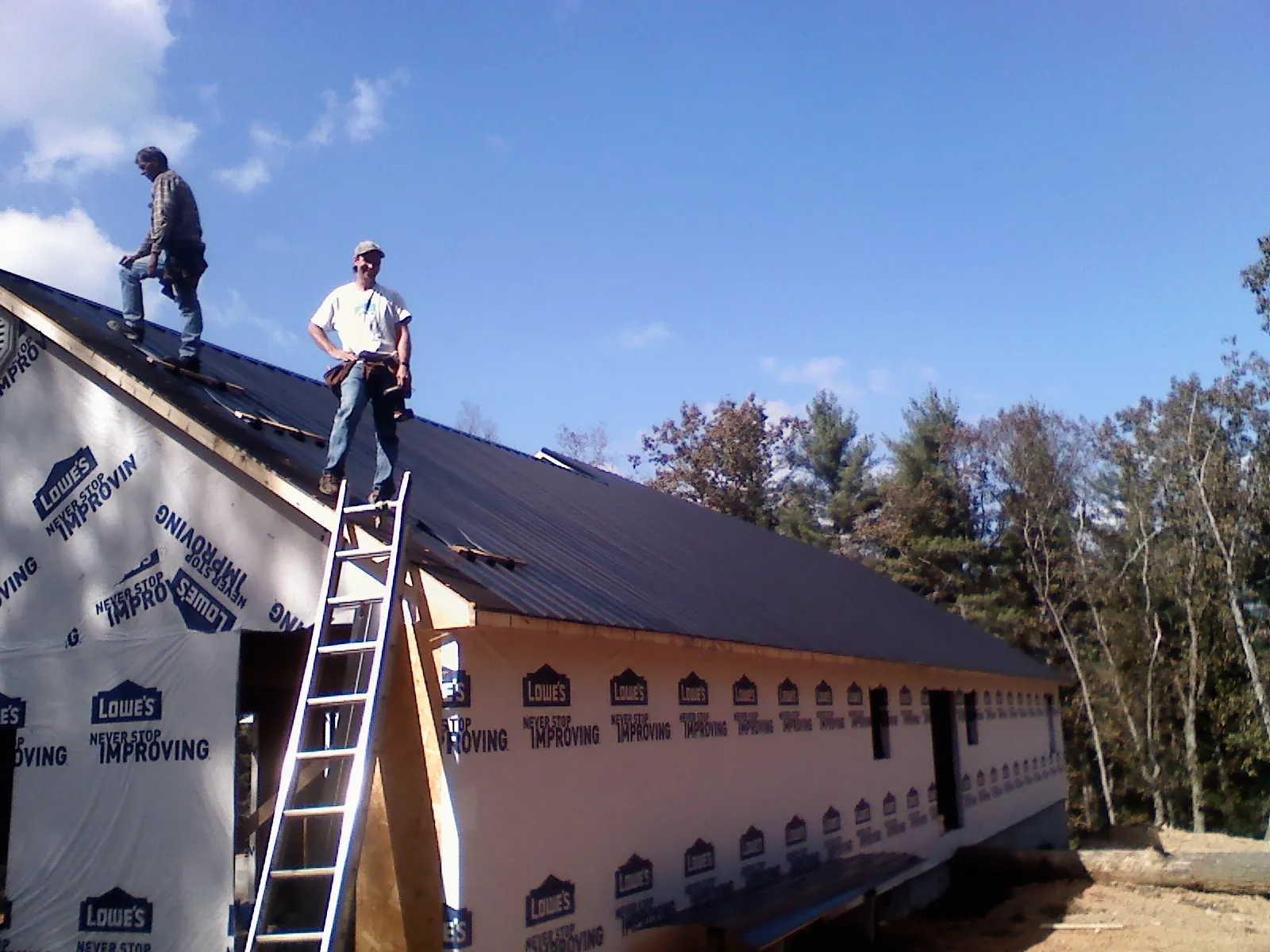 Two roofers standing on a long dark metal roof over a wrapped building in Sun Valley